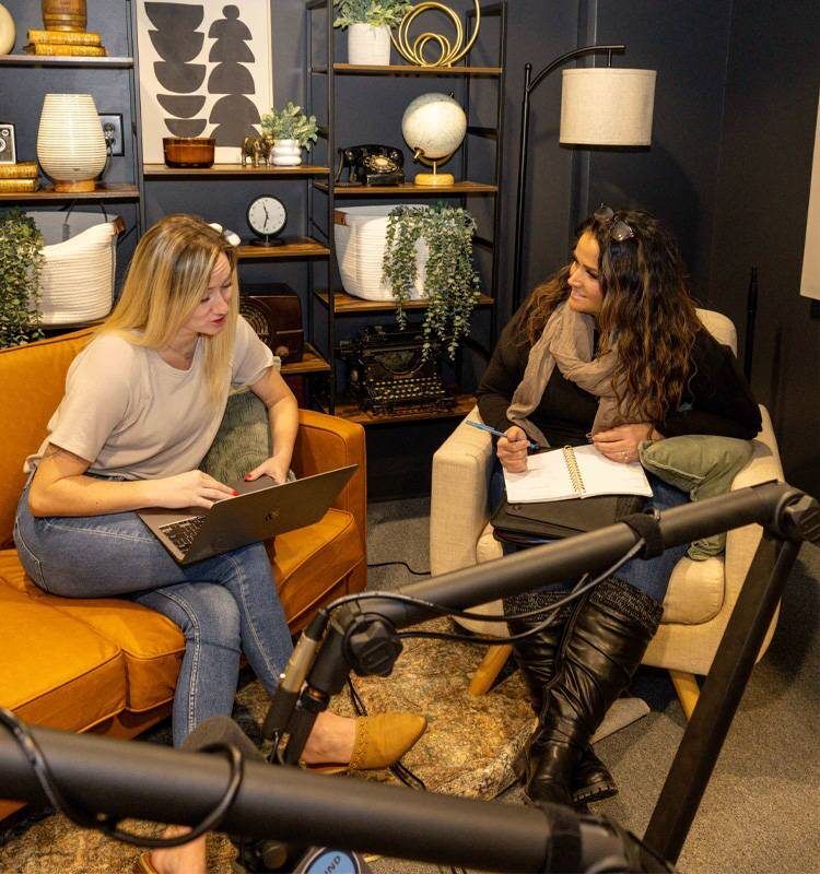 two women sitting on chairs with laptops and a notepad